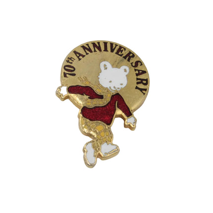A small round gold-tone commemorative pin featuring rupert the bear wearing a red outfit, with the text '70th ANNIVERSARY' around the edge, shown on a plain light background.