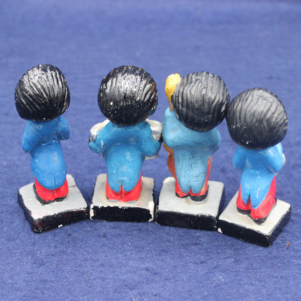 Four small figurines with blue bodies, black hair, and red shoes on a blue background