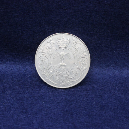 Silver 1977 Queen Elizabeth coin with intricate design on a blue fabric background