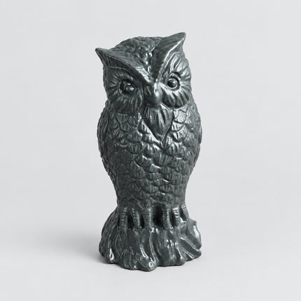 A small owl figurine with textured feathers, standing on a brown surface with a gray fabric background.