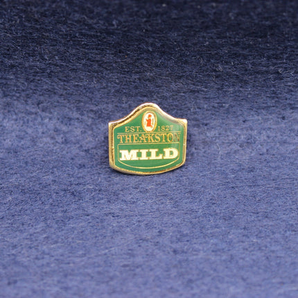 A classic vintage enamel pin celebrating Theakston, featuring a green shield‑shaped design with gold border