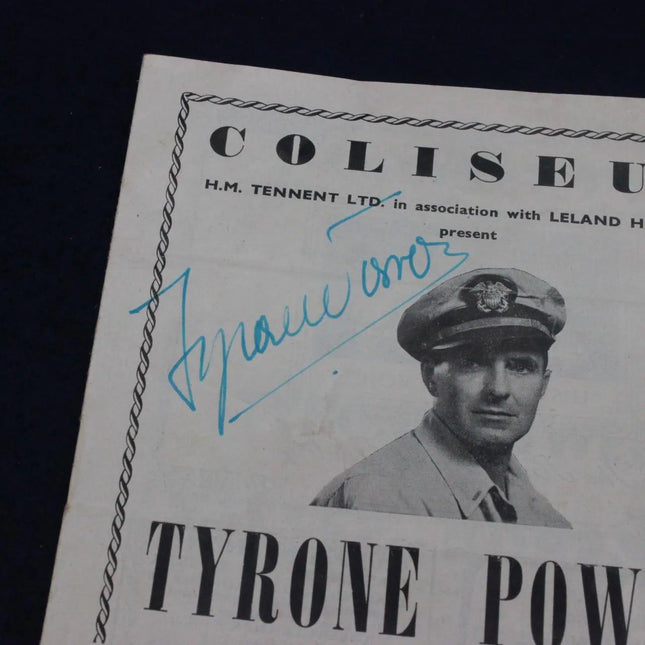 A vintage printed poster or program page featuring a black-and-white portrait of Tyrone Power in a military uniform, with large text reading 'COLISEU' at the top and 'TYRONE POW' at the bottom. The page has a blue handwritten signature across the center and is photographed against a dark background.