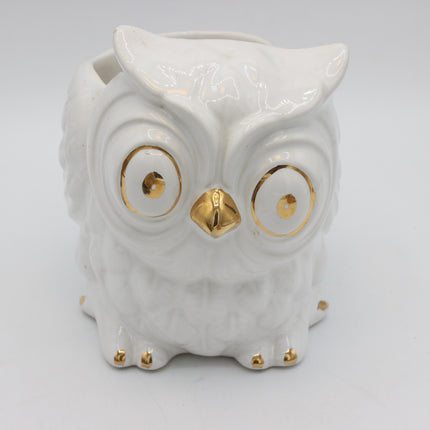 A white ceramic owl figurine with gold accents on its eyes, beak, and feet, photographed against a plain white background.