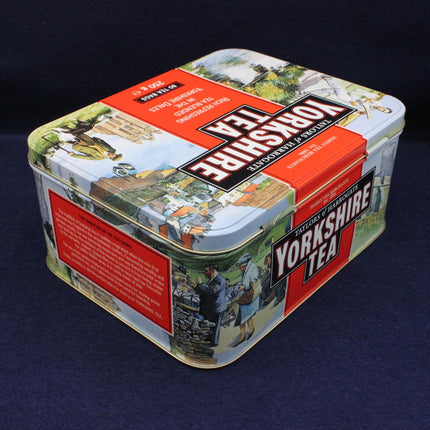 A square metal tin of Yorkshire Tea loose-leaf tea, featuring vintage-style illustrations and bold red and white branding, set against a dark blue background.